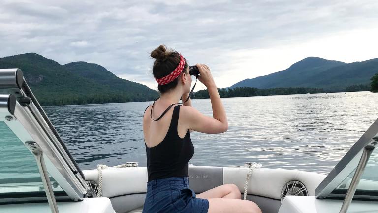 woman looking through binoculars on a boat in the Adirondacks