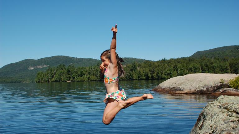little girl jumping into a lake in the Adirondacks during the summer