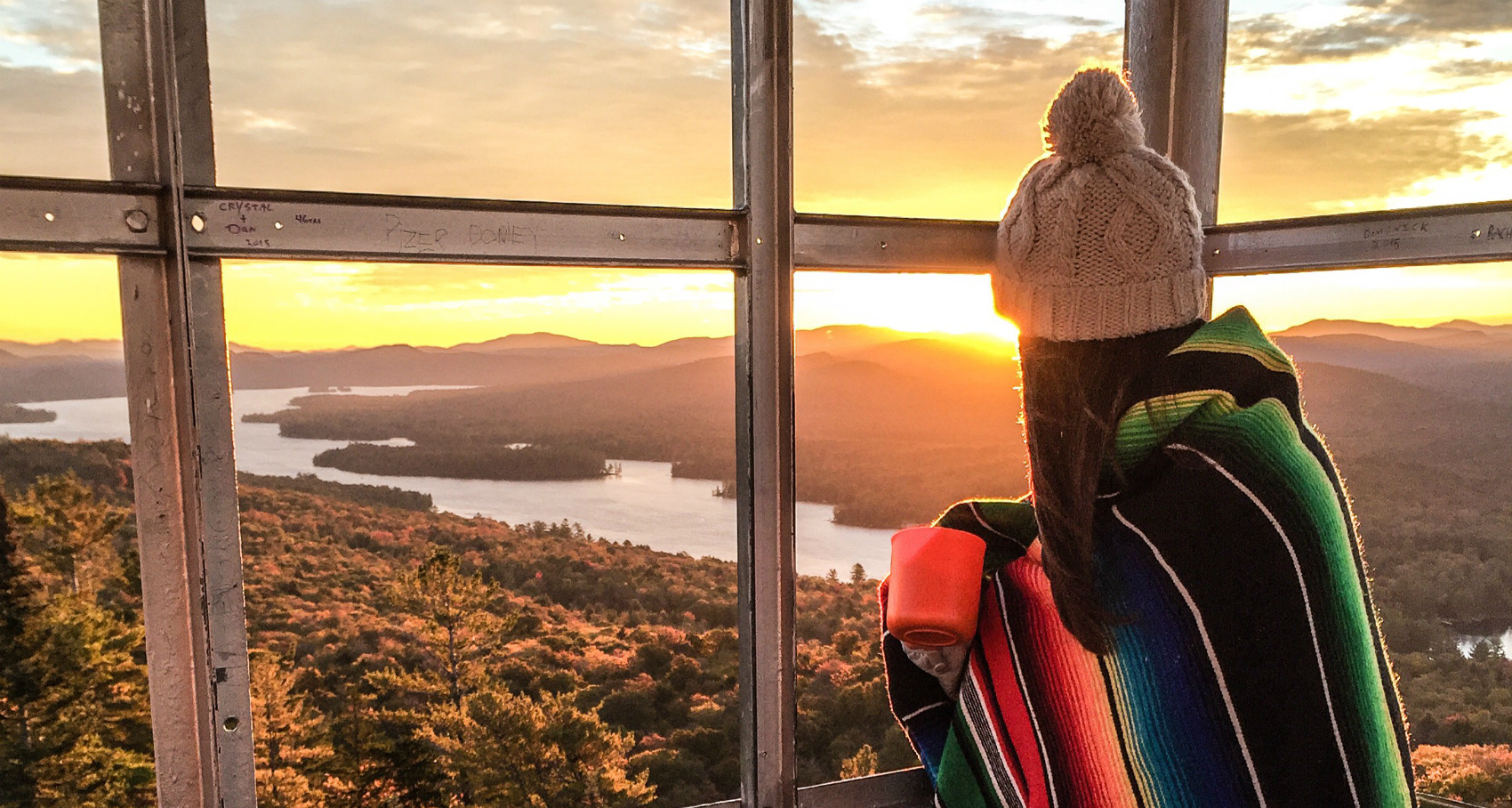 girl in a blanket watching the sunrise from an Adirondack fire tower in Fall