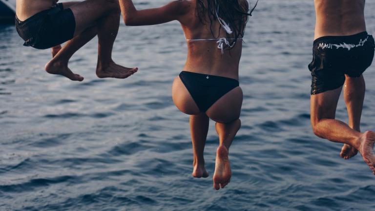 three people jumping into a lake